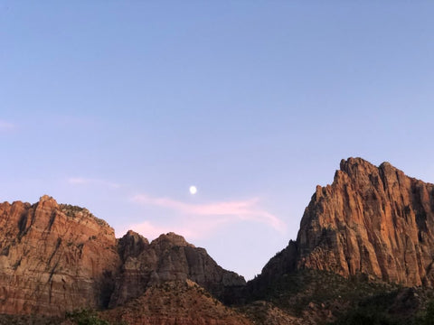 The moon rising above a rocky mountain range.