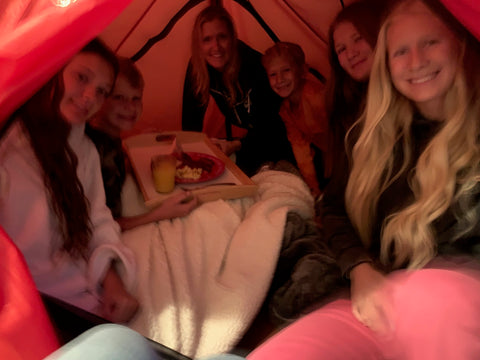 A group of friends huddle together inside a red tent.