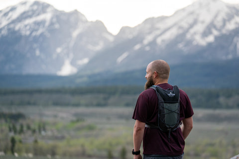 A man faces away from the camera while wearing a TETON Sports TrailRunner 2L Backpack and viewing a snowy mountain range.