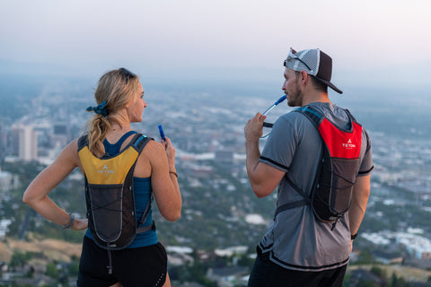 A man and a woman sip from their TETON Sports TrailRunner Hydration Packs while viewing the city from above.