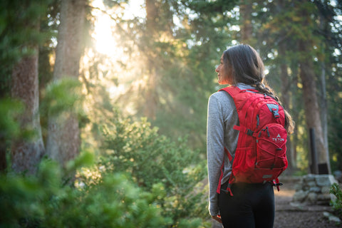 A woman hikes up a log in a forest while wearing a TETON Sports Oasis Backpack.