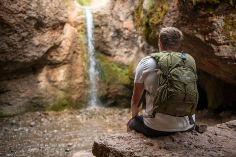 A man wearing a TETON Sports Oasis Backpack stares at a lovely, rocky waterfall.