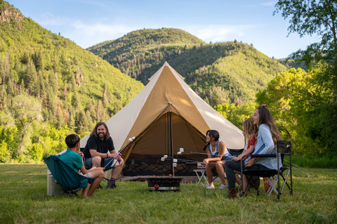 A family huddles around a campfire in front of a TETON Sports Sierra Canvas Bell Tent while roasting marshmallows.