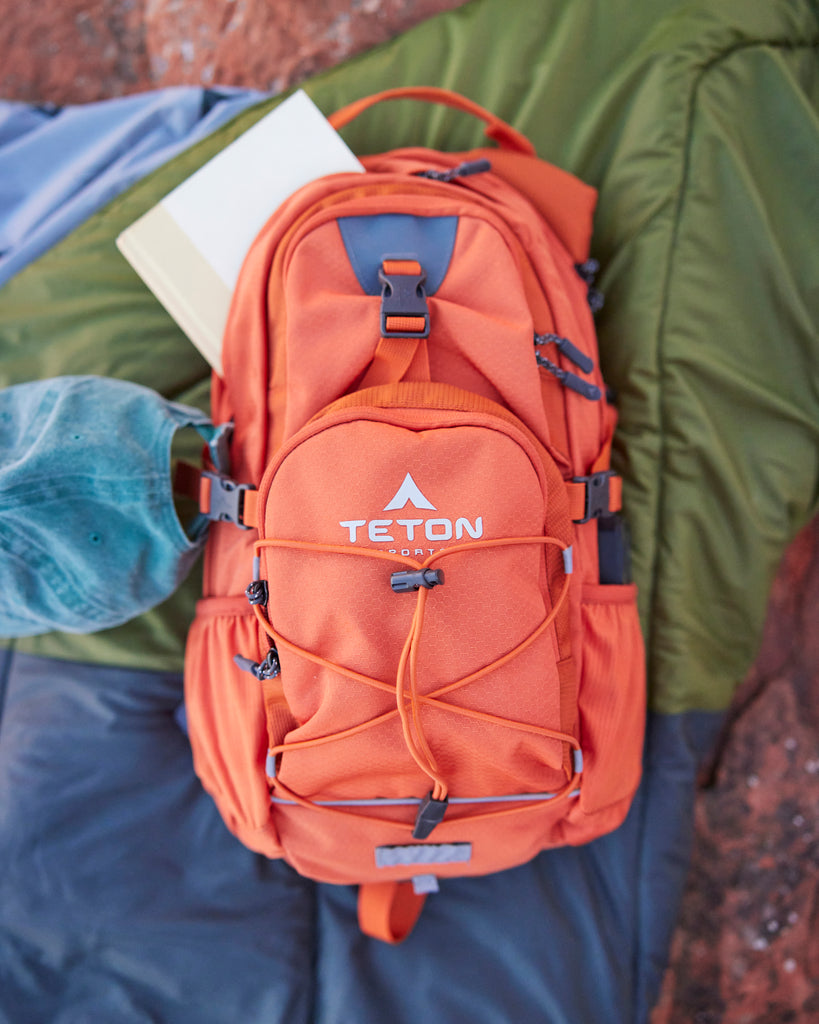 Orange backpack sits on ground face up.