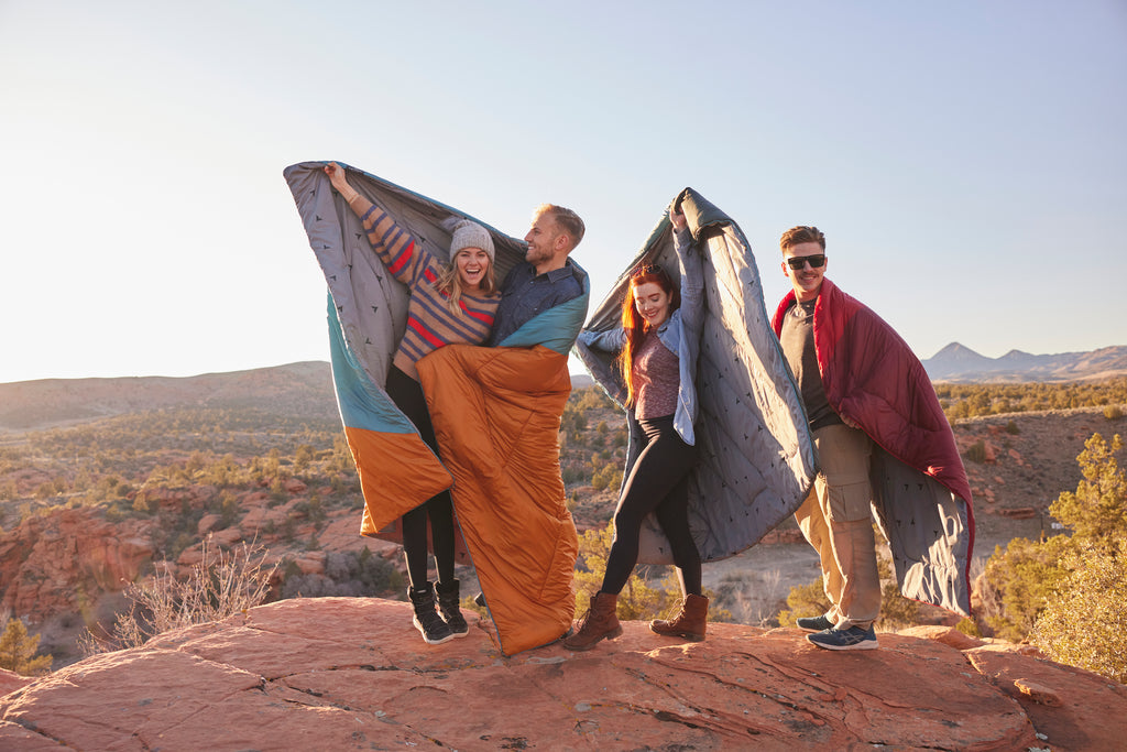 Group of friends stand on rock wrapped in camp blanket.