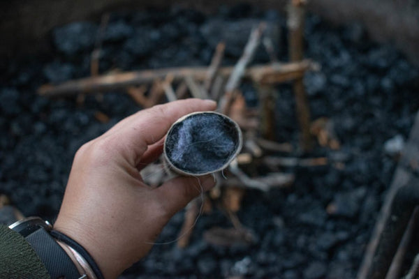 A hand holds a small stone over a campfire.