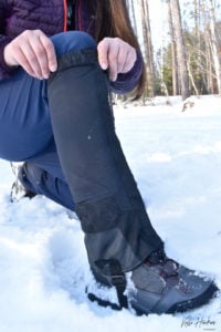 A woman pulls up her snow boots while hiking.