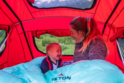 A woman and her child snuggle together into a TETON Sports Cascade Two-Person Sleeping Bag inside a tent.
