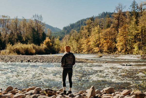 A person gazing over a river in a fall forest scape.