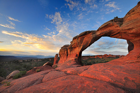 A red rock arch with a view of a cloudy sky in the background.