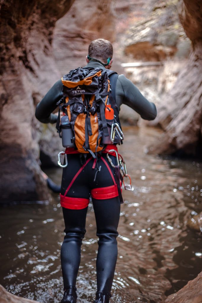 Man stands in water with backpack canyoneering.