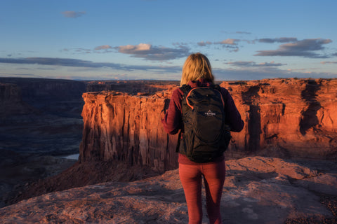 A woman faces away from the camera at dusk wearing a TETON Sports Rock Backpack for hiking.