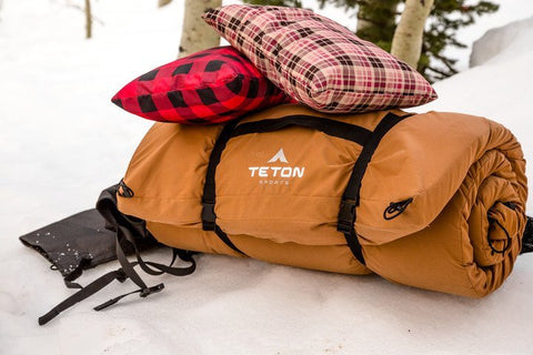 A rolled TETON Sports canvas camping pad is topped with two camping pillows.