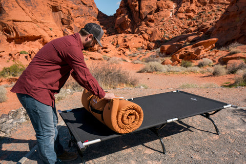 A man unrolls his TETON Sports canvas sleeping pad atop a TETON Sports camp cot.