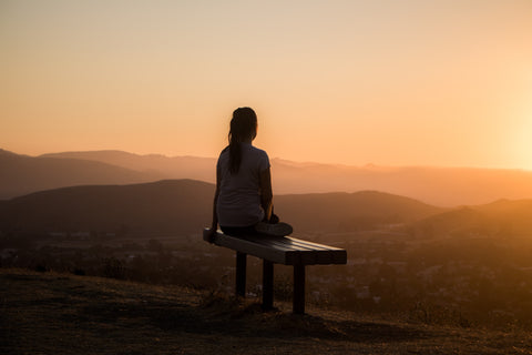 A woman sits alone on a bench at the top of a mountain during sunrise.