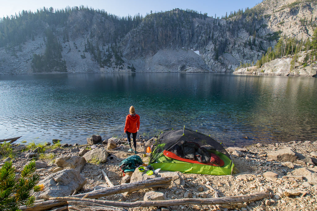 Woman looking out at lake in the morning near tent. 