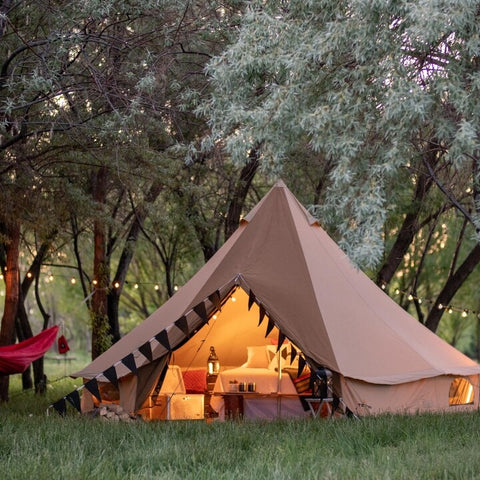 A TETON Sports SIerra Canvas Tent is set-up in a glamping type scene with outdoor lights, a large bed, and a hammock.