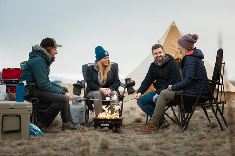 A groupd of friends roasting marshmallows around a campfire in front of a TETON Sports Sierra Tent.