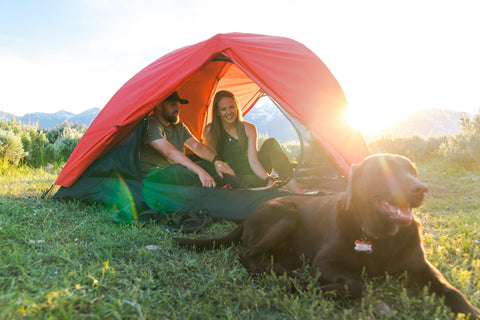 A couple snuggles inside a TETON Sports Mountain Ultra Tent while their dog sits outside.