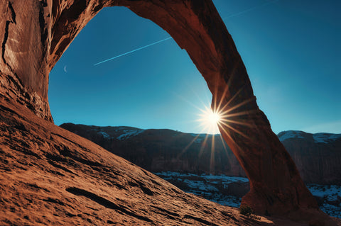 A view of the sun from behind a natural rock arch.