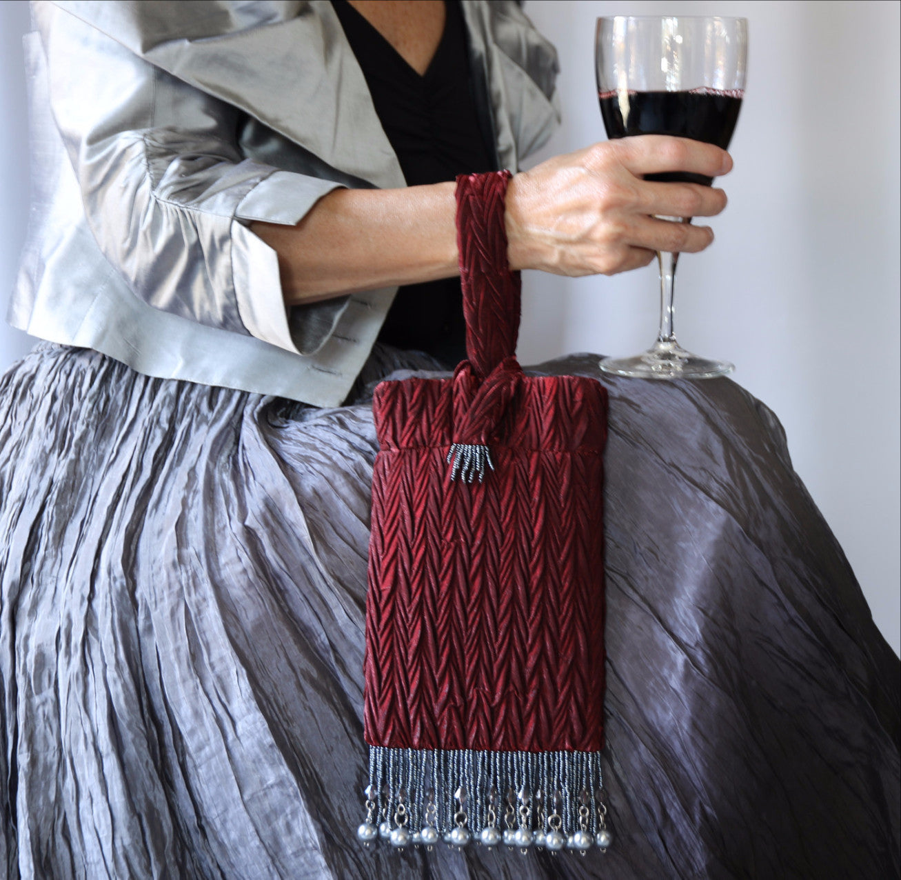 Burgundy Evening Bag from Jenny Jag-Wear Design. Image of  a woman demonstrating how the bag slips onto ladies' wrist, keeping hands free to hold a glass of wine. The Zara Collection by Jenny Jag-Wear Design 