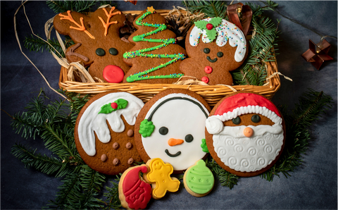 Image of festive gingerbread biscuits in a wicker basket. A reindeer, Christmas tree and Mrs Claus biscuit sit in the basket and a Christmas pudding, snowman and Santa Claus biscuit sit in front of the basket along with three mini, iced shortbread character biscuits.