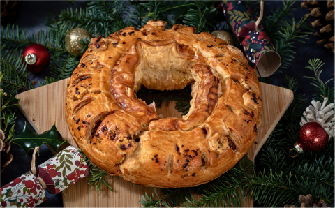 Pastry wreath on a star-shaped wooden board, surrounded by festive greenery, baubles, and a Christmas cracker