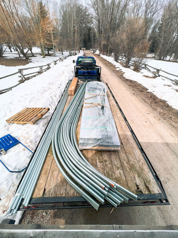 A fully disassembled Rimol Rolling Thunder greenhouse sitting on a flatbed trailer on a snowy rural road.