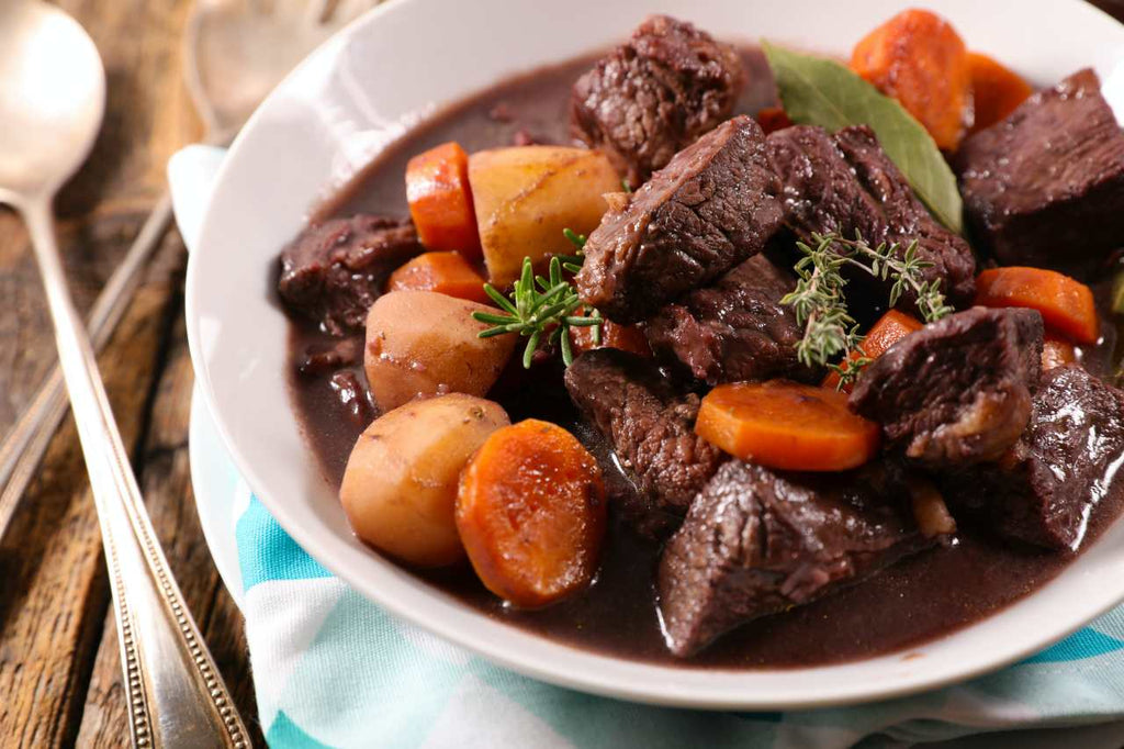 cooked beef bone broth with meat, potato and carrots on a white dish with spoon