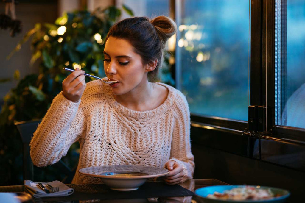 woman sipping on bone broth using spoon with her hand on a bowl