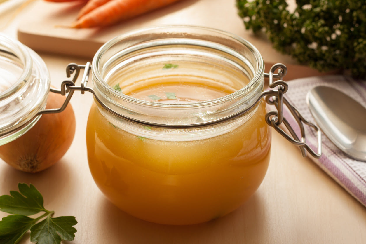 bone broth made from chicken in a glass jar with carrots onions and celery root in the background
