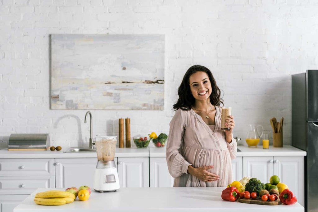 happy pregnant woman holding glass with smoothie near table