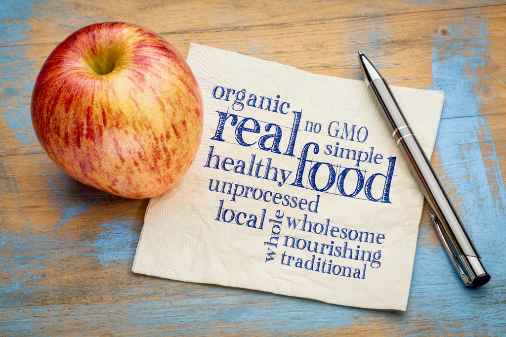 An organic apple beside a pen and paper with written words about unprocessed real food