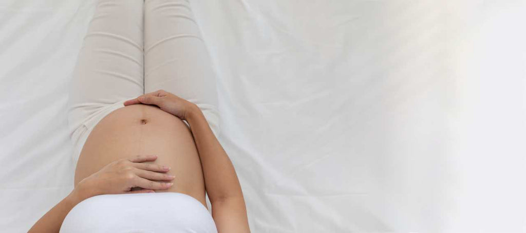 top view of a happy pregnant woman sitting on bed holding and stroking her big belly