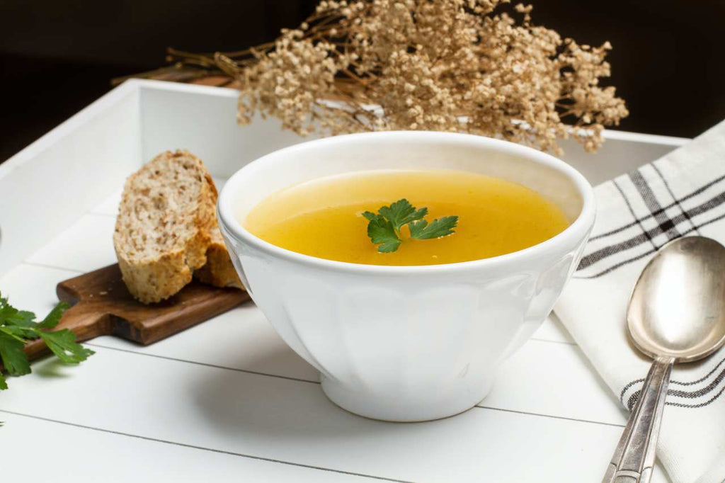 vegetable mineral broth in a white bowl with spoon and bread