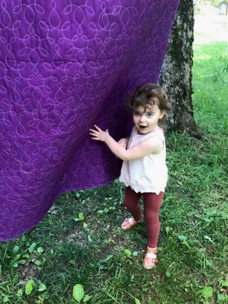 Pippa peeking from behind a quilt which is hanging on a clothes line