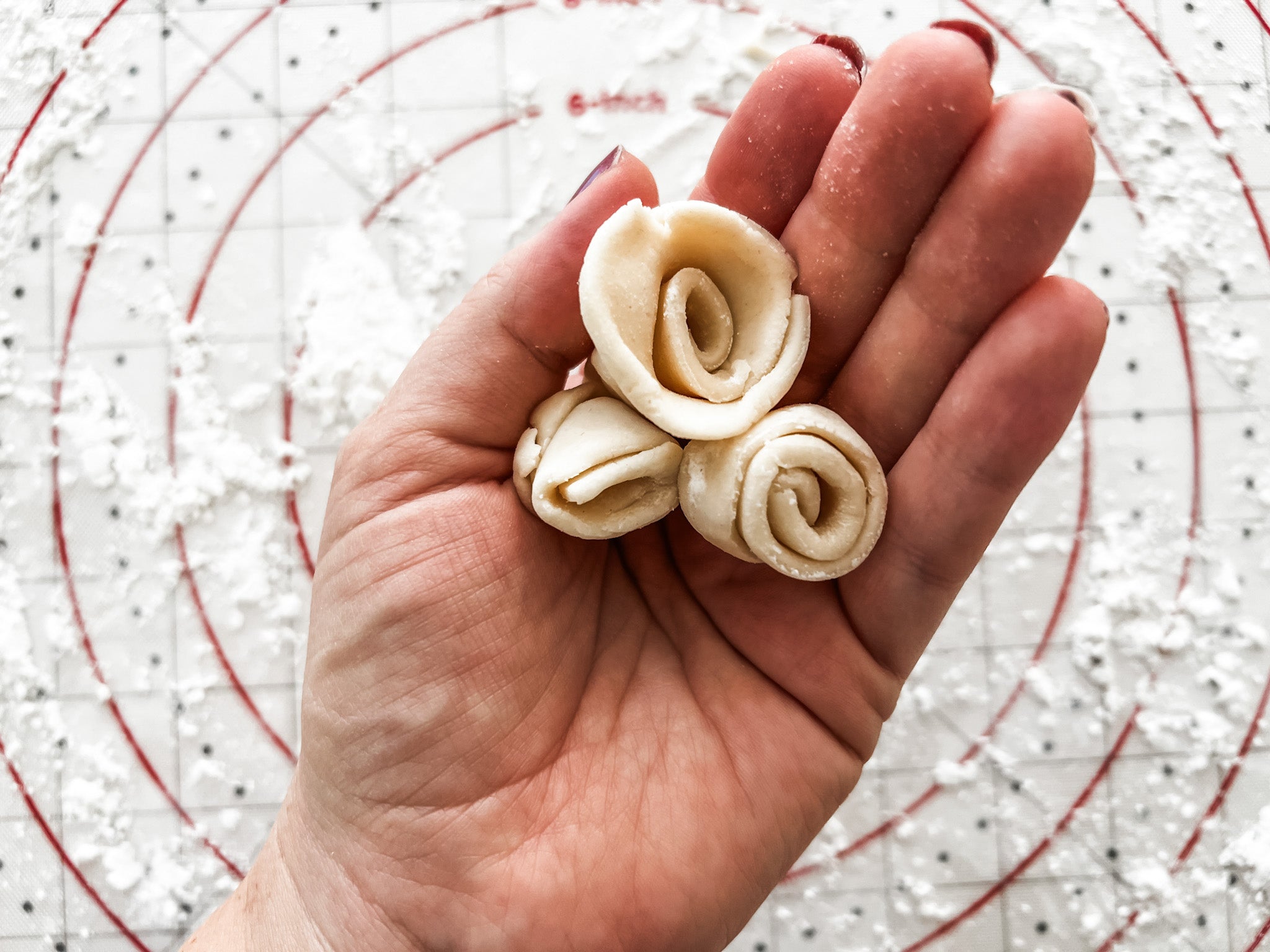 pie crust rosettes in my hand over a floured silicone pastry mat background