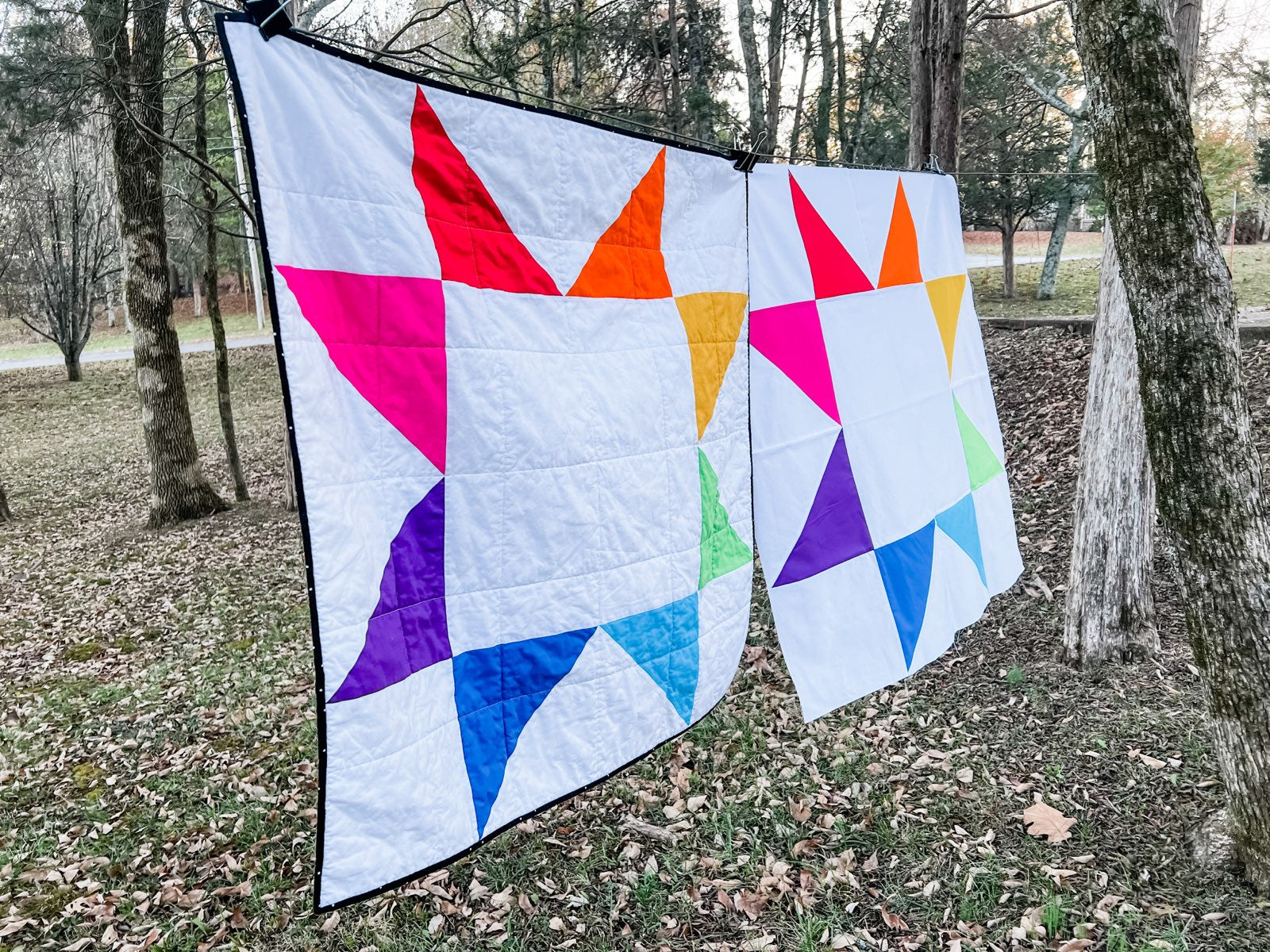 Two Rainbow sawtooth star quilts hanging on a line outside