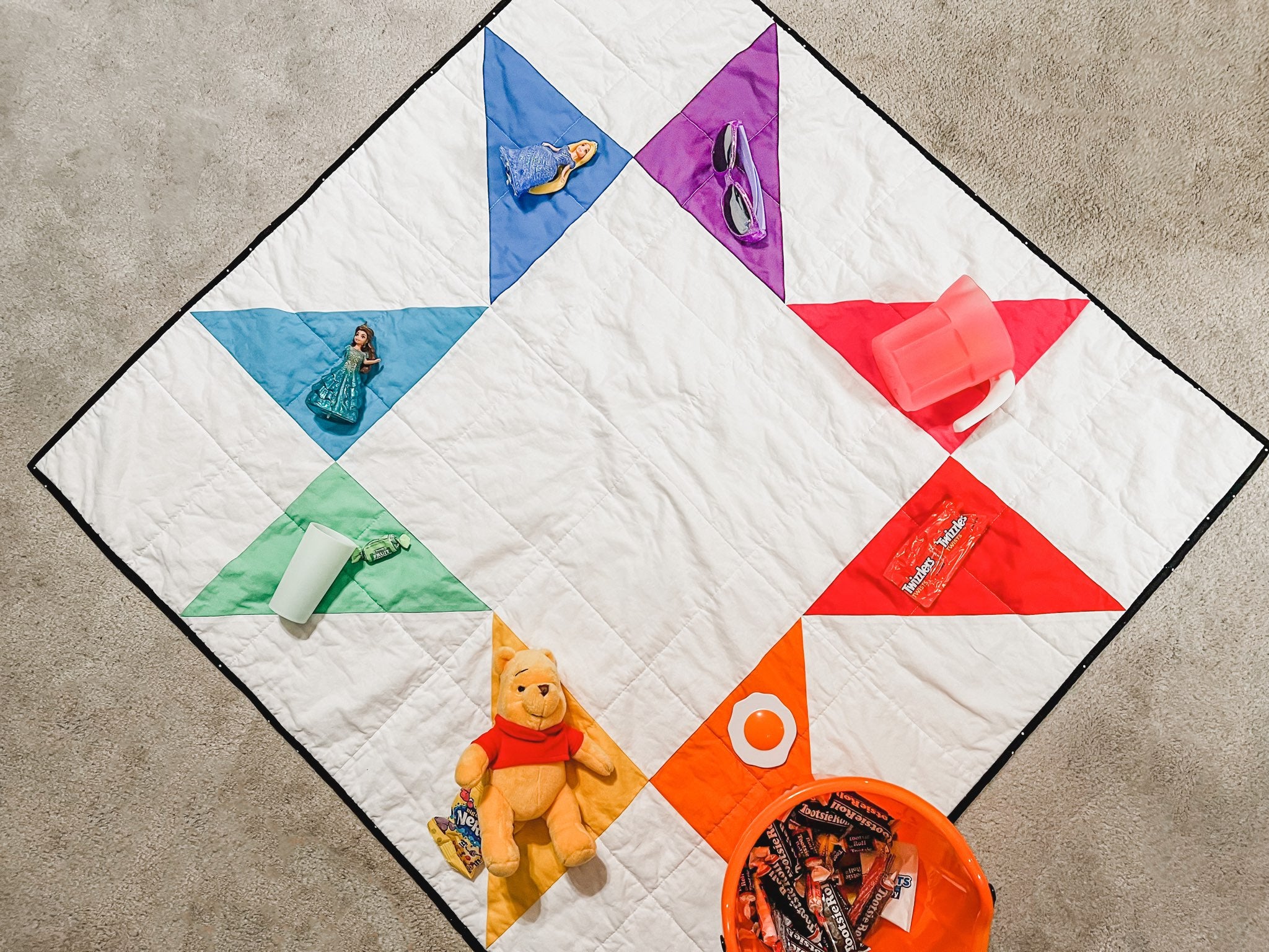 rainbow sawtooth star quilt on the floor with matching toys placed over each color