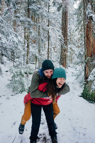 Guy riding piggyback on fiance in snowy forest
