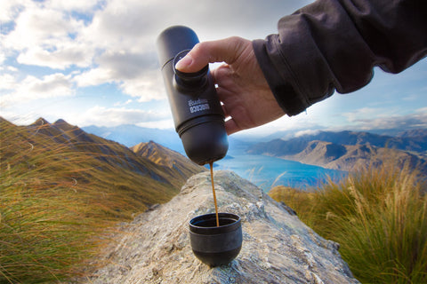 mini handheld espresso maker pouring coffee in the mountains by a lake