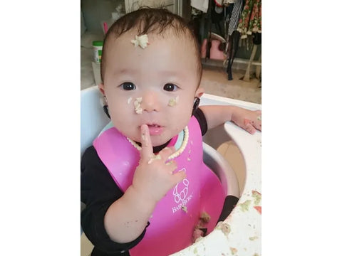 両耳に乳幼児用補聴器をつけてご飯を食べる明凛ちゃんの写真
