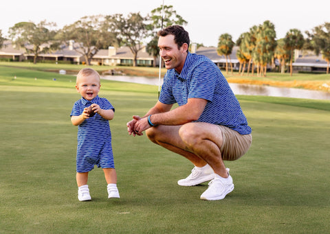 a toddler boy and father are on a golf course modeling blue striped onesie and blue striped golf polo