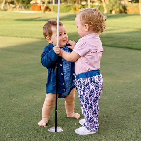 Two toddlers wearing pink and blue golf outfits model their clothes on a golf course.