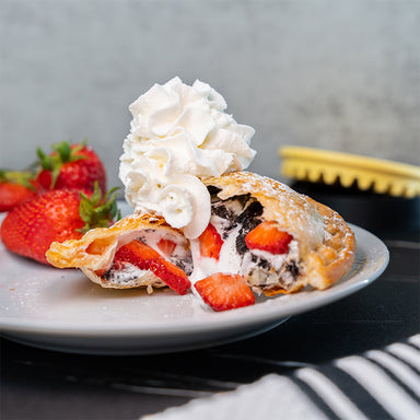 A toasted snack filled with oreos, cream and strawberries. The snack is topped with whipped cream.