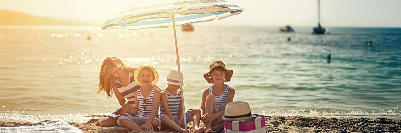 Mutter mit Kindern am Strand unter einem Sonnenschirm. Sie genießen die Zeit am Strand