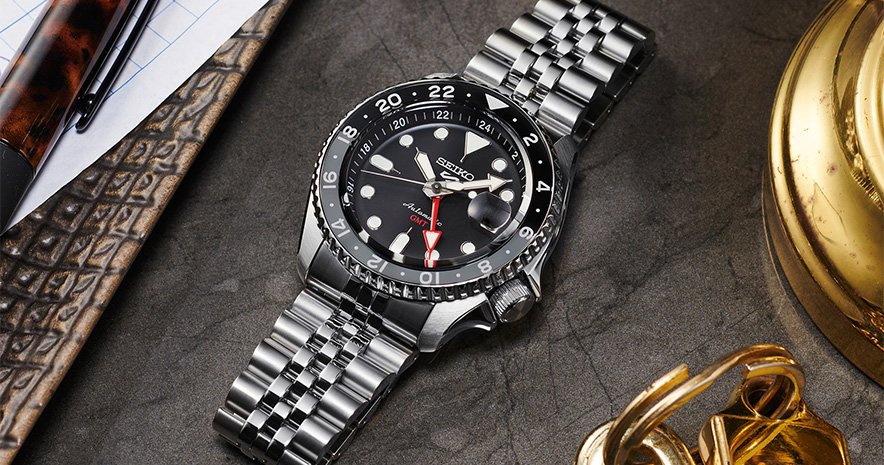 Seiko GMT. Black and Grey bezel with a polished steel bracelet set on dark table.