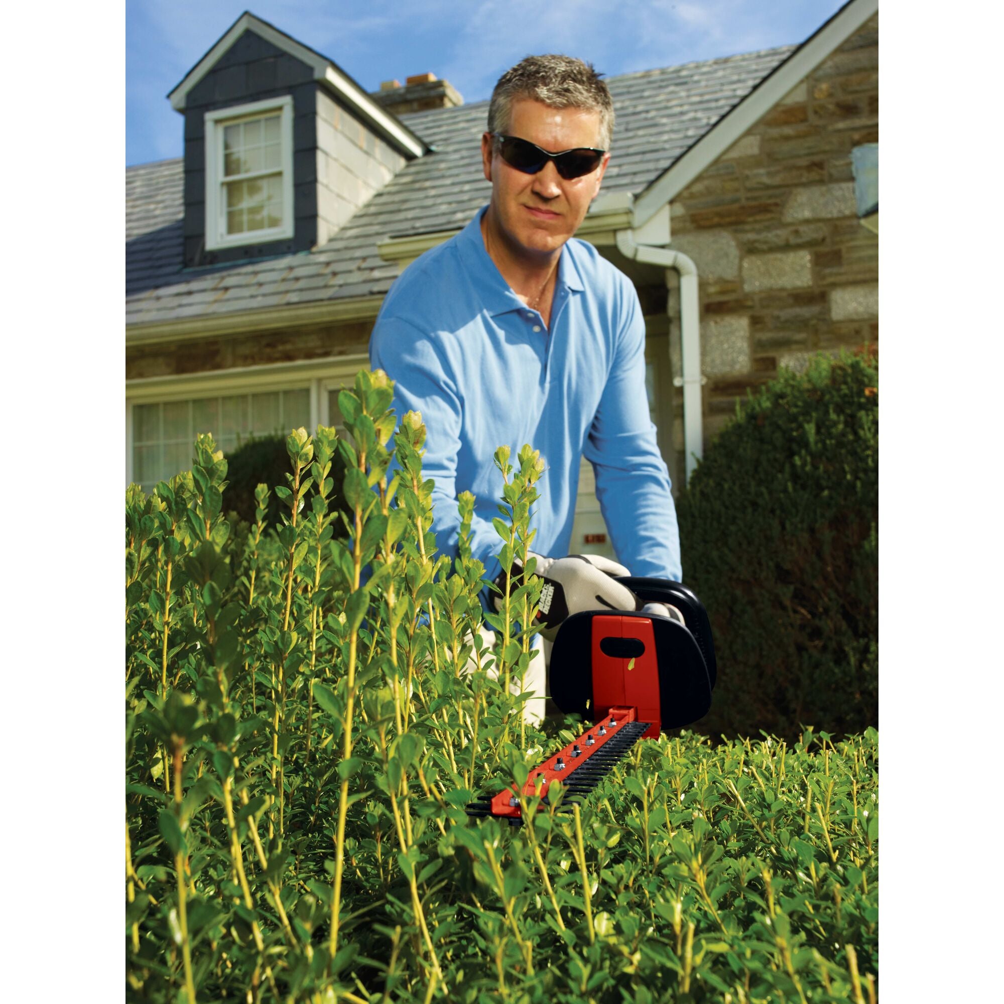 Hedge trimmer with rotating handle being used by a person to trim bushes.