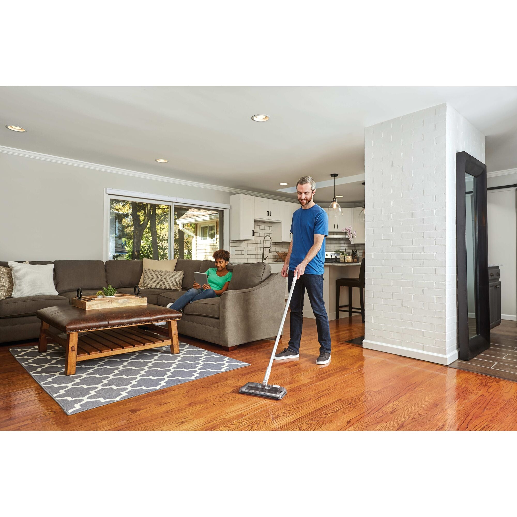 50 Minute Powered Floor Sweeper standing vertically in kitchen beside a person enjoying enjoying beverage.