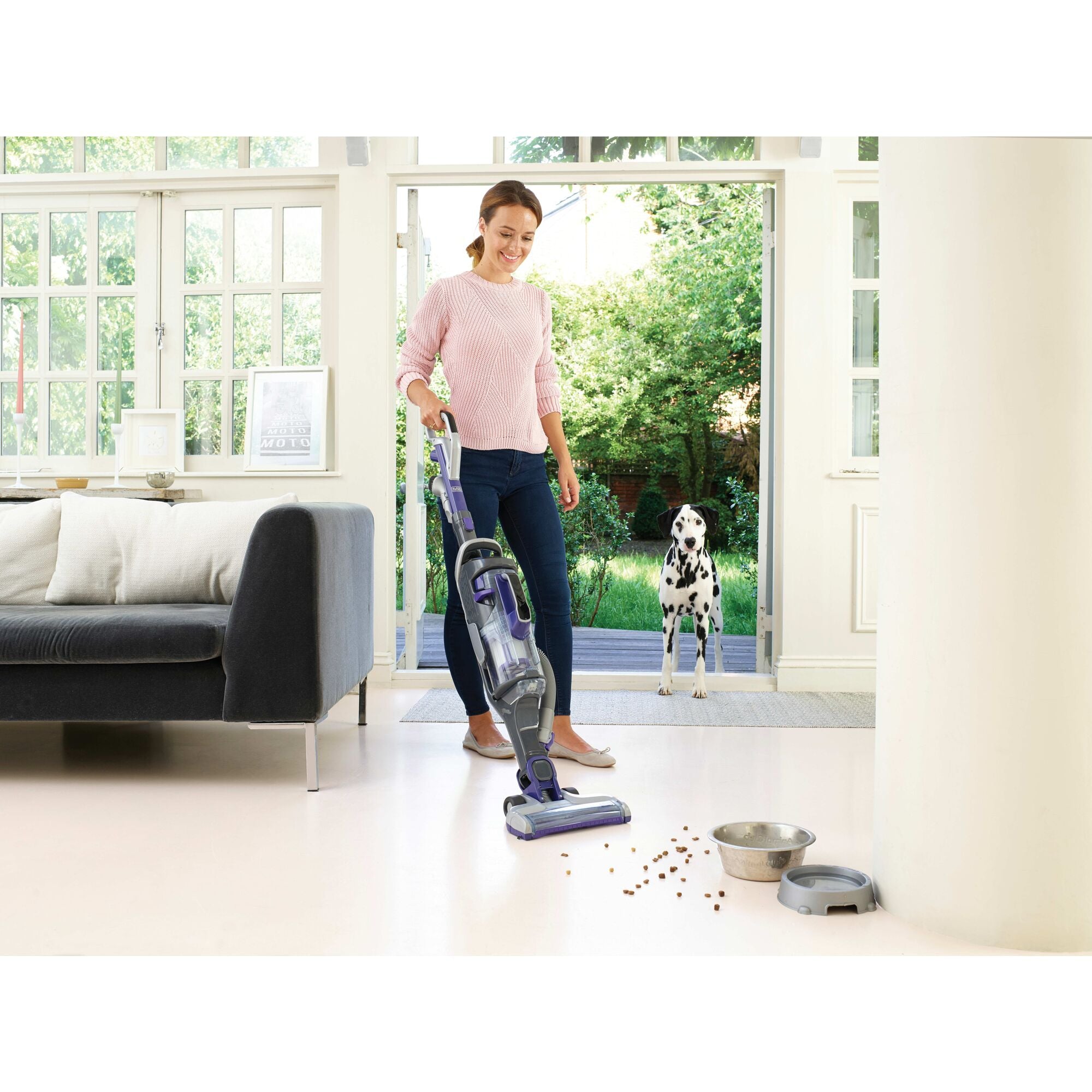 A woman is using the BLACK+DECKER POWERSERIES™ Pro Pet Cordless Stick Vacuum Cleaner for cleaning spilled dog food.